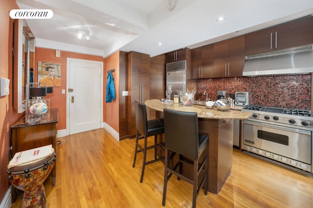 kitchen with a breakfast bar area, high end appliances, a center island, light hardwood / wood-style floors, and decorative backsplash