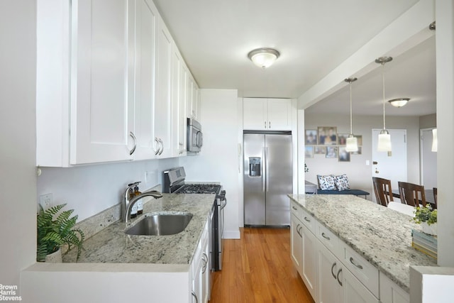 kitchen featuring appliances with stainless steel finishes, white cabinetry, wood-type flooring, sink, and hanging light fixtures