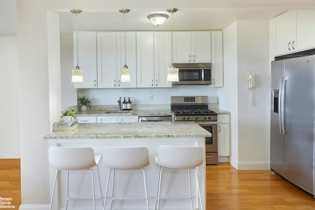 kitchen featuring decorative light fixtures, white cabinets, light hardwood / wood-style floors, light stone counters, and stainless steel appliances