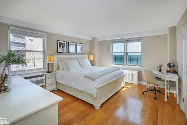 bedroom featuring an AC wall unit, radiator, and light wood-type flooring