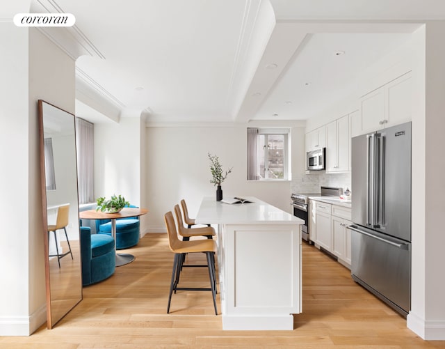 kitchen with tasteful backsplash, white cabinetry, a kitchen breakfast bar, light hardwood / wood-style floors, and stainless steel appliances