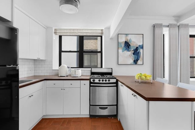 kitchen with sink, stainless steel gas stove, black fridge, backsplash, and white cabinets