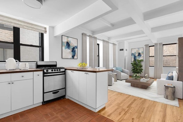 kitchen with gas stove, white cabinets, beam ceiling, and kitchen peninsula