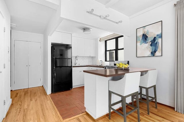 kitchen featuring a breakfast bar, tasteful backsplash, white cabinetry, kitchen peninsula, and black fridge