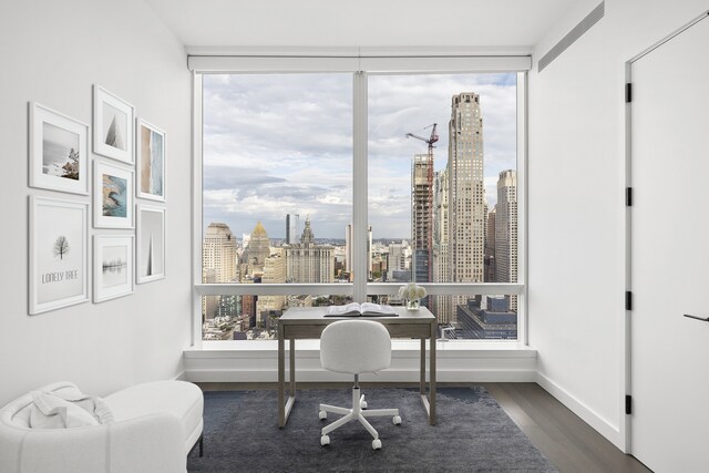 office with dark wood-style floors, a view of city, a wall of windows, and baseboards