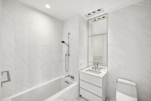 full bath with vanity, tile walls, toilet, and a combined bath / shower with marble appearance