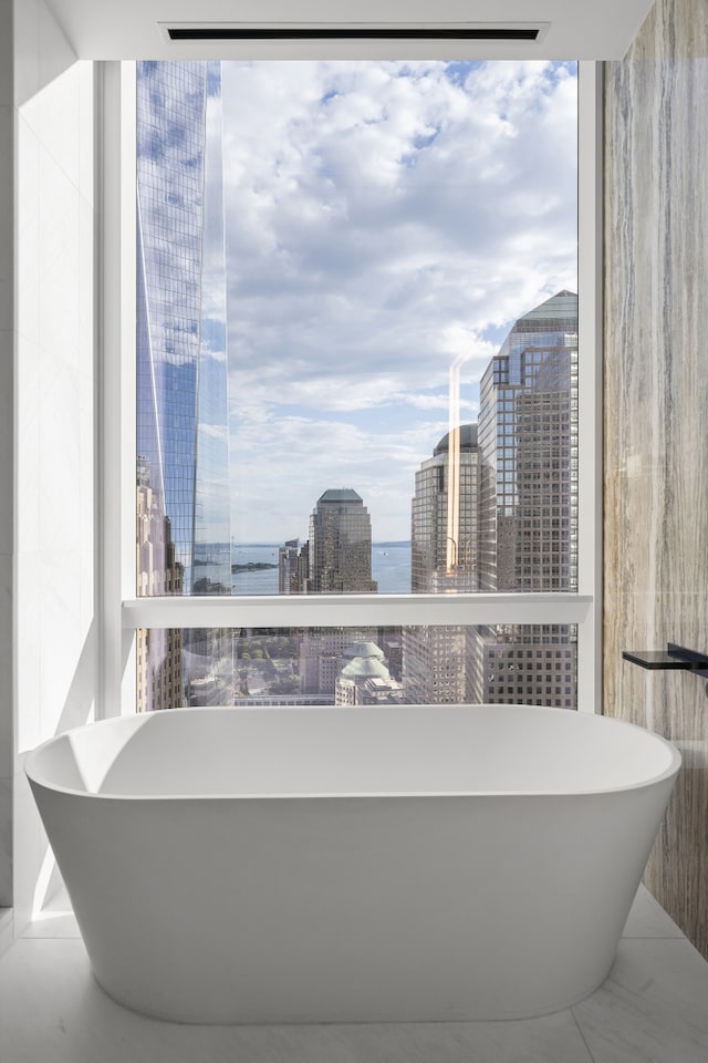 full bath featuring a water view, a freestanding tub, and a view of city