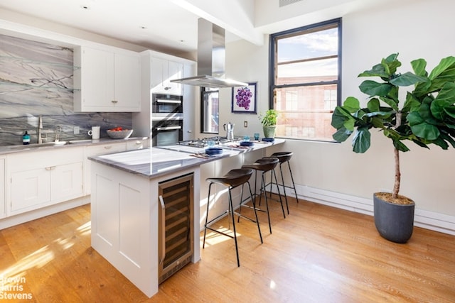 kitchen featuring white cabinetry, island range hood, kitchen peninsula, beverage cooler, and sink