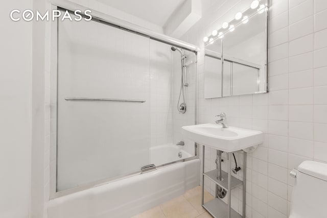 full bathroom with bath / shower combo with glass door, a sink, tile patterned floors, toilet, and tile walls