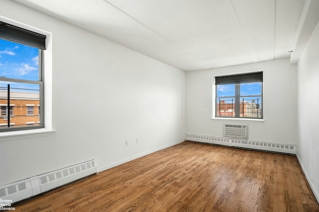 spare room featuring a baseboard radiator, baseboards, wood finished floors, and an AC wall unit