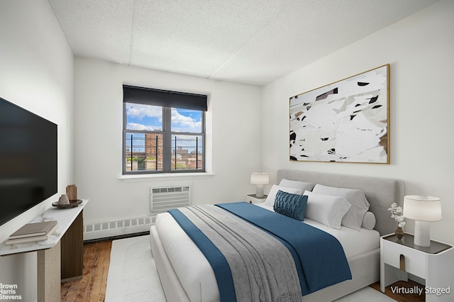 bedroom featuring a wall unit AC, a textured ceiling, baseboard heating, and wood finished floors