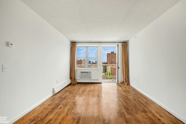 unfurnished room featuring a baseboard radiator, a city view, wood finished floors, baseboards, and a wall mounted AC