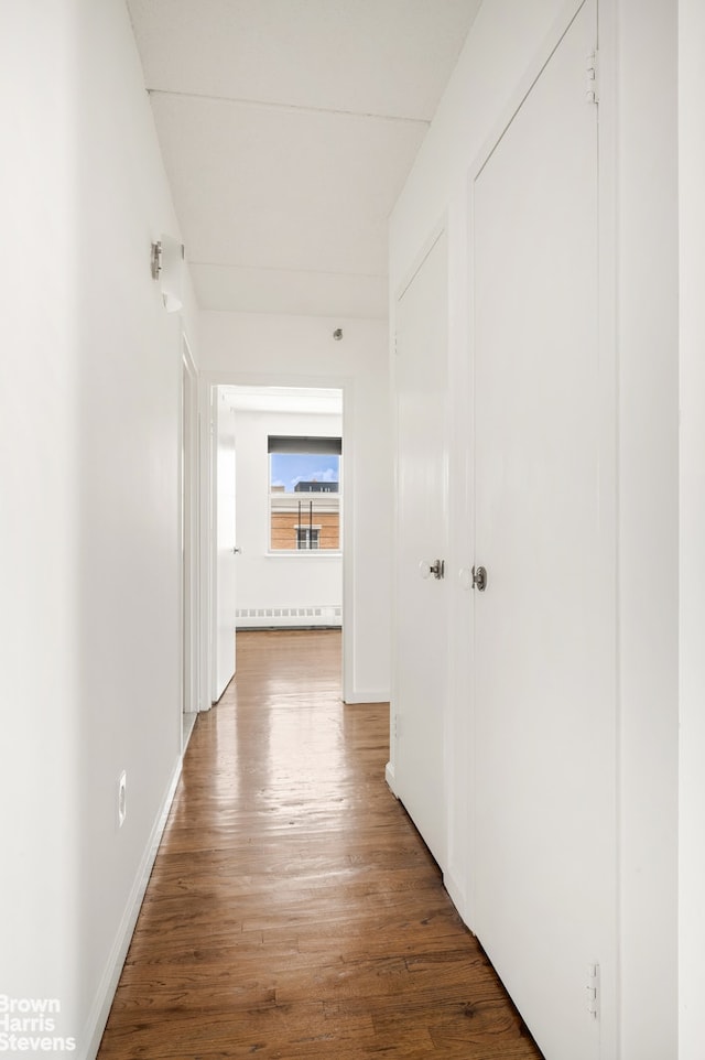 corridor with a baseboard radiator, baseboards, and wood finished floors