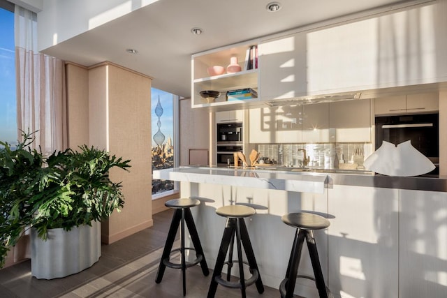 kitchen with sink, dark wood-type flooring, double oven, a kitchen breakfast bar, and tasteful backsplash