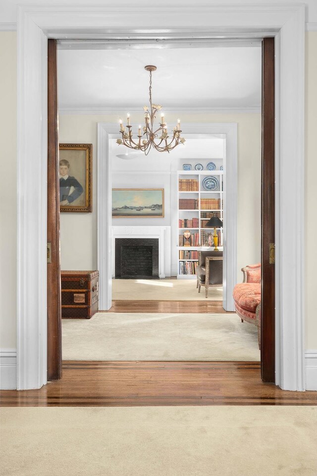 interior space with ornamental molding, a fireplace, an inviting chandelier, and wood finished floors