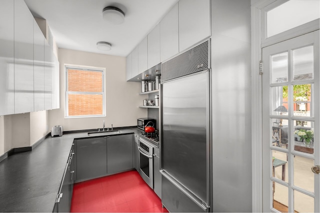 kitchen with dark countertops, appliances with stainless steel finishes, white cabinets, and a sink