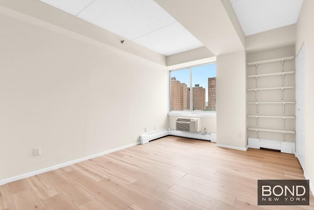 interior space with built in shelves, a baseboard radiator, a wall mounted air conditioner, and light hardwood / wood-style flooring