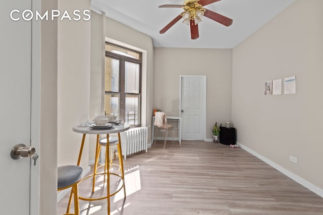 interior space with a ceiling fan, radiator, wood finished floors, and baseboards