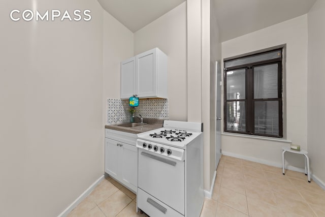 kitchen with a sink, gas range gas stove, backsplash, white cabinetry, and light tile patterned floors