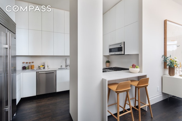 kitchen with stainless steel appliances, modern cabinets, dark wood-type flooring, a kitchen bar, and white cabinetry