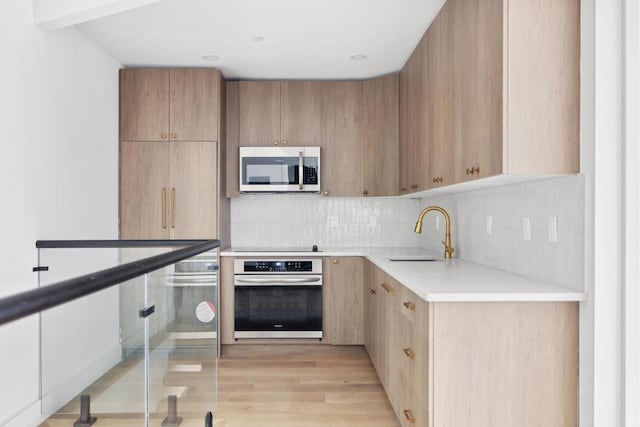 kitchen with sink, decorative backsplash, light hardwood / wood-style floors, and appliances with stainless steel finishes