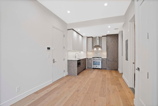 kitchen with tasteful backsplash, sink, stainless steel range, light hardwood / wood-style floors, and wall chimney range hood