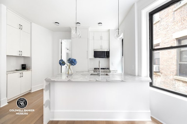 kitchen with sink, white cabinetry, hanging light fixtures, light stone countertops, and kitchen peninsula