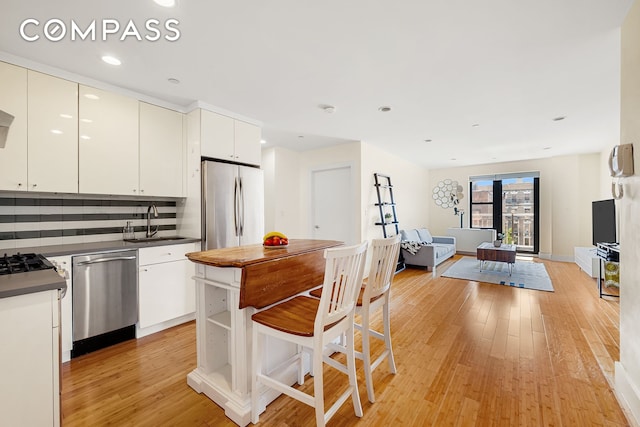 kitchen with a sink, open floor plan, appliances with stainless steel finishes, light wood finished floors, and tasteful backsplash