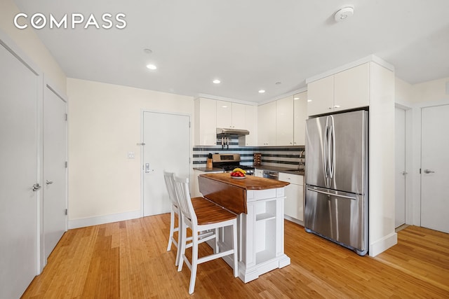 kitchen with stainless steel appliances, under cabinet range hood, white cabinets, light wood-style floors, and recessed lighting