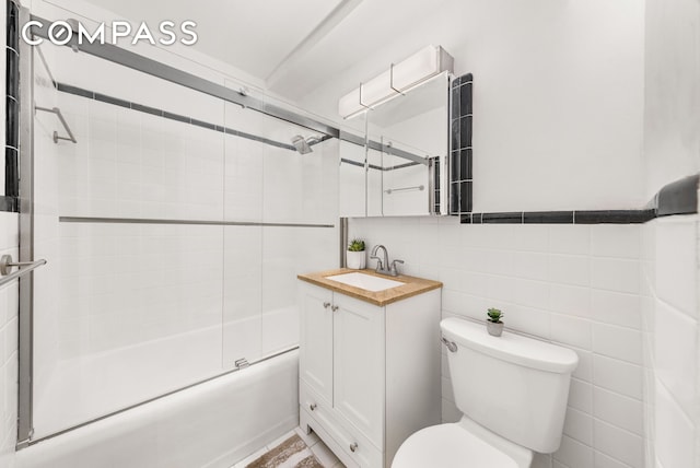 bathroom with toilet, combined bath / shower with glass door, tile walls, and vanity