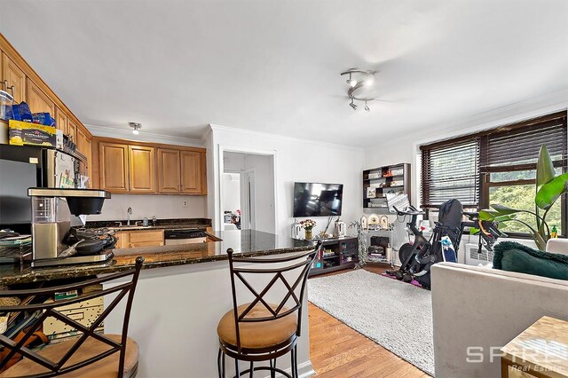 kitchen with dark stone countertops, a kitchen breakfast bar, ornamental molding, kitchen peninsula, and light wood-type flooring