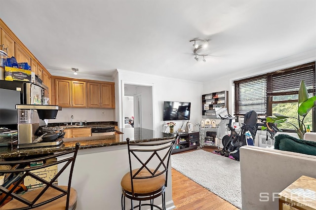 kitchen featuring light wood finished floors, open floor plan, a kitchen bar, ornamental molding, and a peninsula