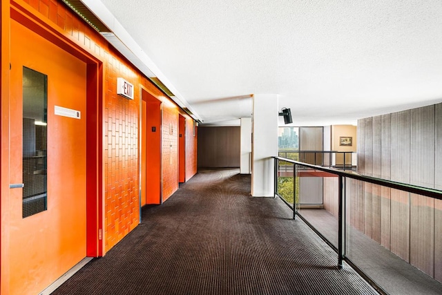 corridor with elevator, a textured ceiling, dark carpet, and wood walls