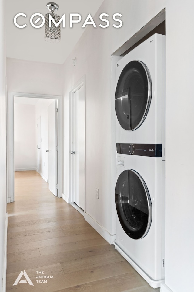 washroom featuring laundry area, wood finished floors, baseboards, and stacked washing maching and dryer