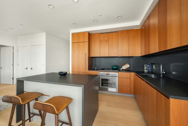 kitchen featuring a kitchen island, tasteful backsplash, sink, oven, and light hardwood / wood-style flooring