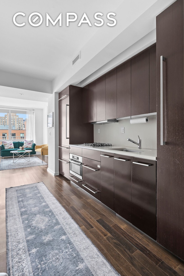 kitchen with dark wood-style floors, dark brown cabinetry, light countertops, oven, and modern cabinets