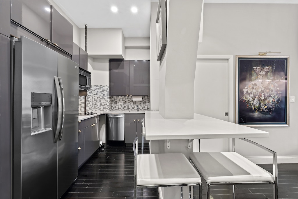 kitchen with appliances with stainless steel finishes, a peninsula, light countertops, dark wood-type flooring, and a breakfast bar area