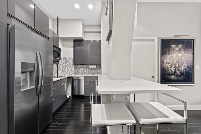 kitchen with appliances with stainless steel finishes, a peninsula, light countertops, dark wood-type flooring, and a breakfast bar area