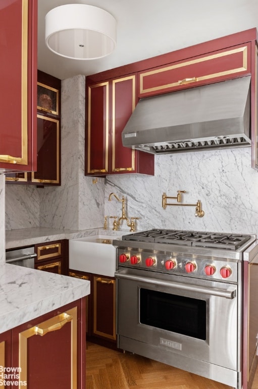 kitchen with wall chimney exhaust hood, light parquet flooring, premium range, light stone countertops, and backsplash