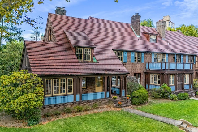 rear view of house featuring a yard, brick siding, a chimney, and a porch