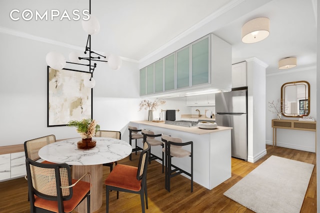 kitchen with wood finished floors, a peninsula, appliances with stainless steel finishes, and crown molding