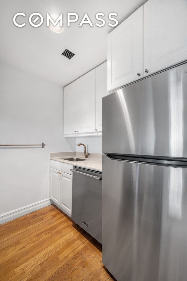 kitchen with white cabinetry, stainless steel appliances, a sink, light wood finished floors, and visible vents