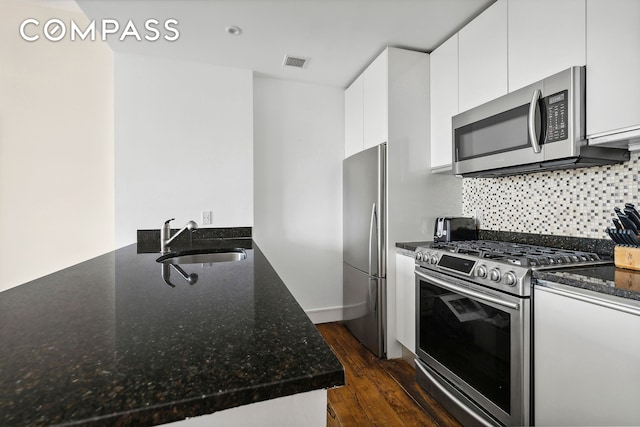 kitchen with visible vents, white cabinets, dark stone countertops, stainless steel appliances, and a sink