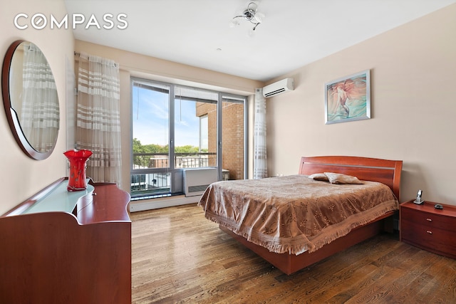 bedroom with a baseboard radiator, an AC wall unit, wood finished floors, and access to outside