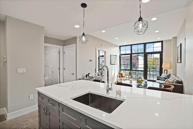 kitchen with light stone counters, sink, and hanging light fixtures