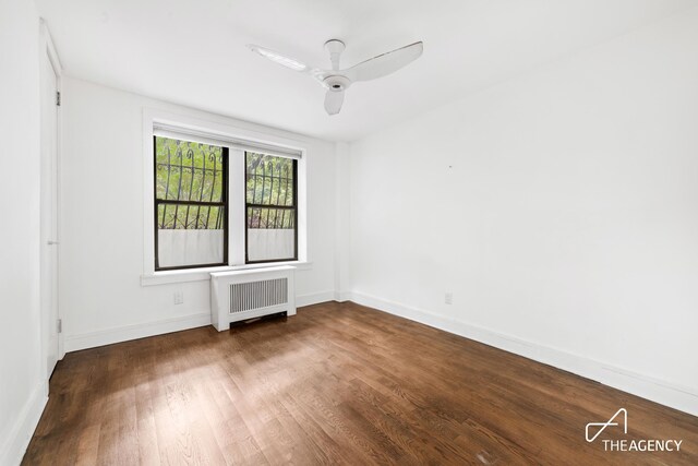 empty room featuring ceiling fan, dark hardwood / wood-style floors, and radiator heating unit