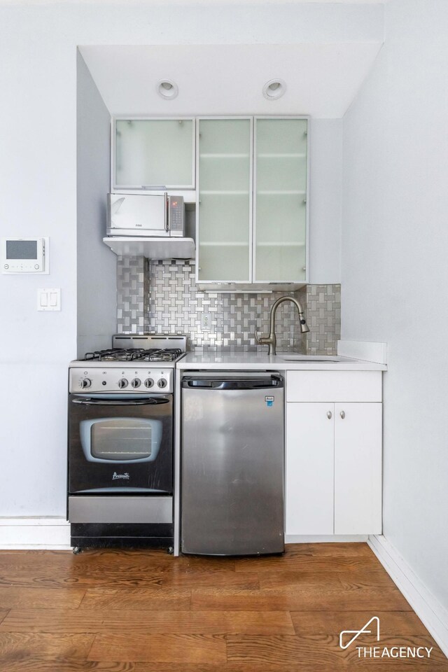 kitchen featuring decorative backsplash, stainless steel gas stove, white cabinets, and dishwashing machine