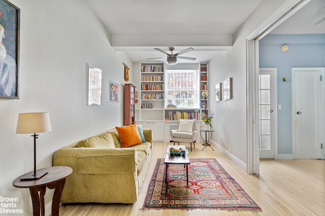 living room featuring built in shelves, light hardwood / wood-style flooring, and ceiling fan