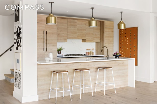 kitchen with a sink, light brown cabinetry, light wood finished floors, a kitchen bar, and tasteful backsplash