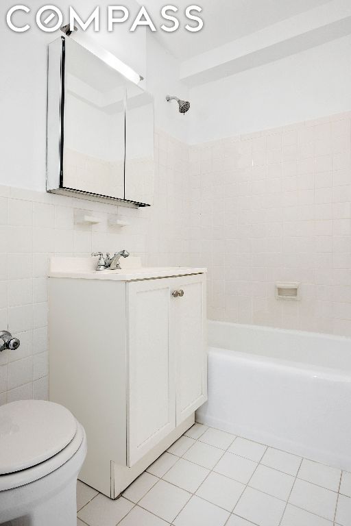 full bathroom with tile walls, vanity, tile patterned floors, toilet, and tiled shower / bath